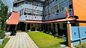 A multi-story building with a red-tiled roof, large windows, and a flag. - Emerald Coast Hotel Negombo (Kochchikade)