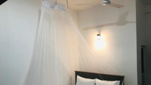 A bedroom with a bed, white bedding, a ceiling fan, and a wall-mounted light fixture. - Emerald Coast Hotel Negombo (Kochchikade)