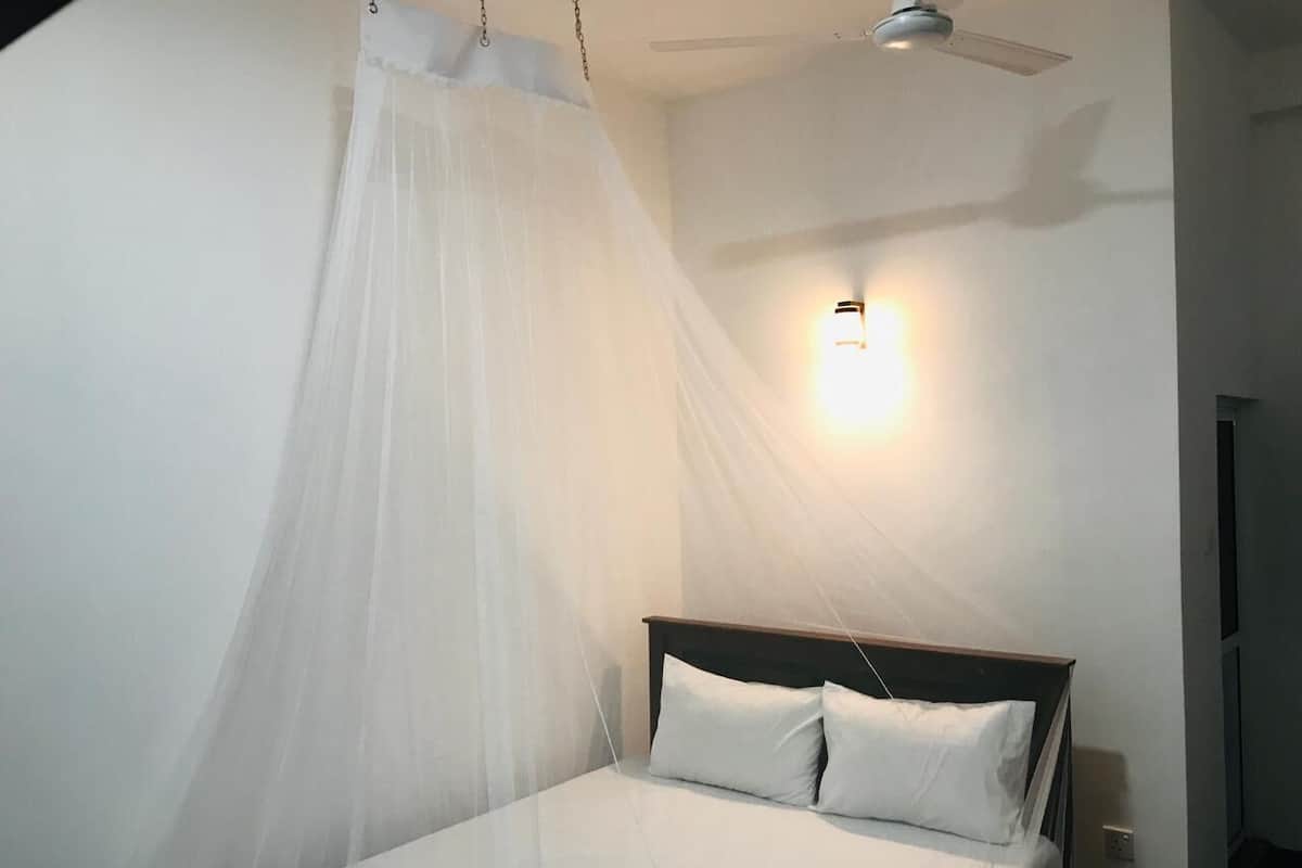 A bedroom with a bed, white bedding, a ceiling fan, and a wall-mounted light fixture.