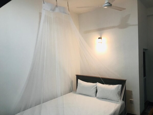 A bedroom with a bed, white bedding, a ceiling fan, and a wall-mounted light fixture. - Emerald Coast Hotel Negombo (Kochchikade)