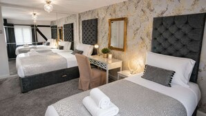 Habitación de hotel con tres camas, un escritorio, una silla y un espejo grande.