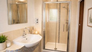 Ein Badezimmer mit einer gläsernen Duschkabine, einem Waschbecken mit Spiegel und einer Topfpflanze.