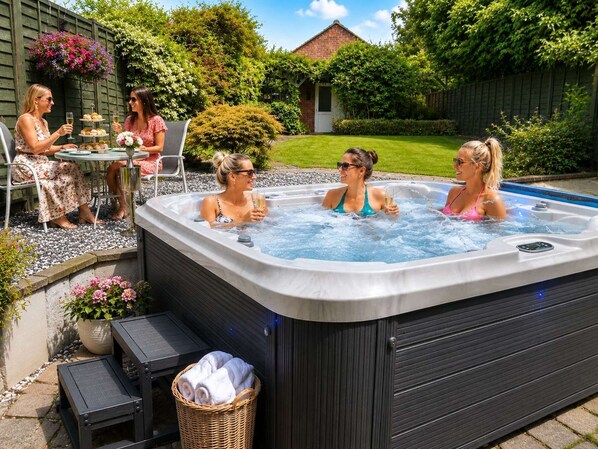 Un jacuzzi con cuatro personas, una mesa con bebidas y un jardín al fondo.