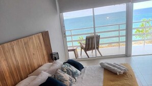 A bedroom with a large bed, a wooden headboard, a view of the ocean, and a balcony with a chair. - STEPHENS HOUSE, 7 color ocean front San Andres Islands. (San Andrés y Providencia)