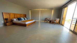 A modern bedroom with a large bed, a wooden headboard, a nightstand, and a seating area with chairs and a table. - STEPHENS HOUSE, 7 color ocean front San Andres Islands. (San Andrés y Providencia)