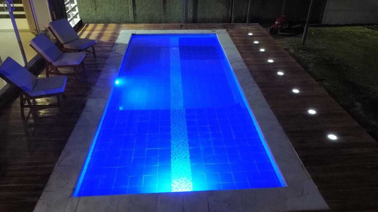 A rectangular swimming pool with a blue illuminated edge, surrounded by a paved deck with evenly spaced lights.