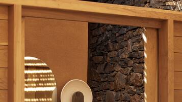 Un baño con pared de piedra, puerta de madera, espejo y lavabo.