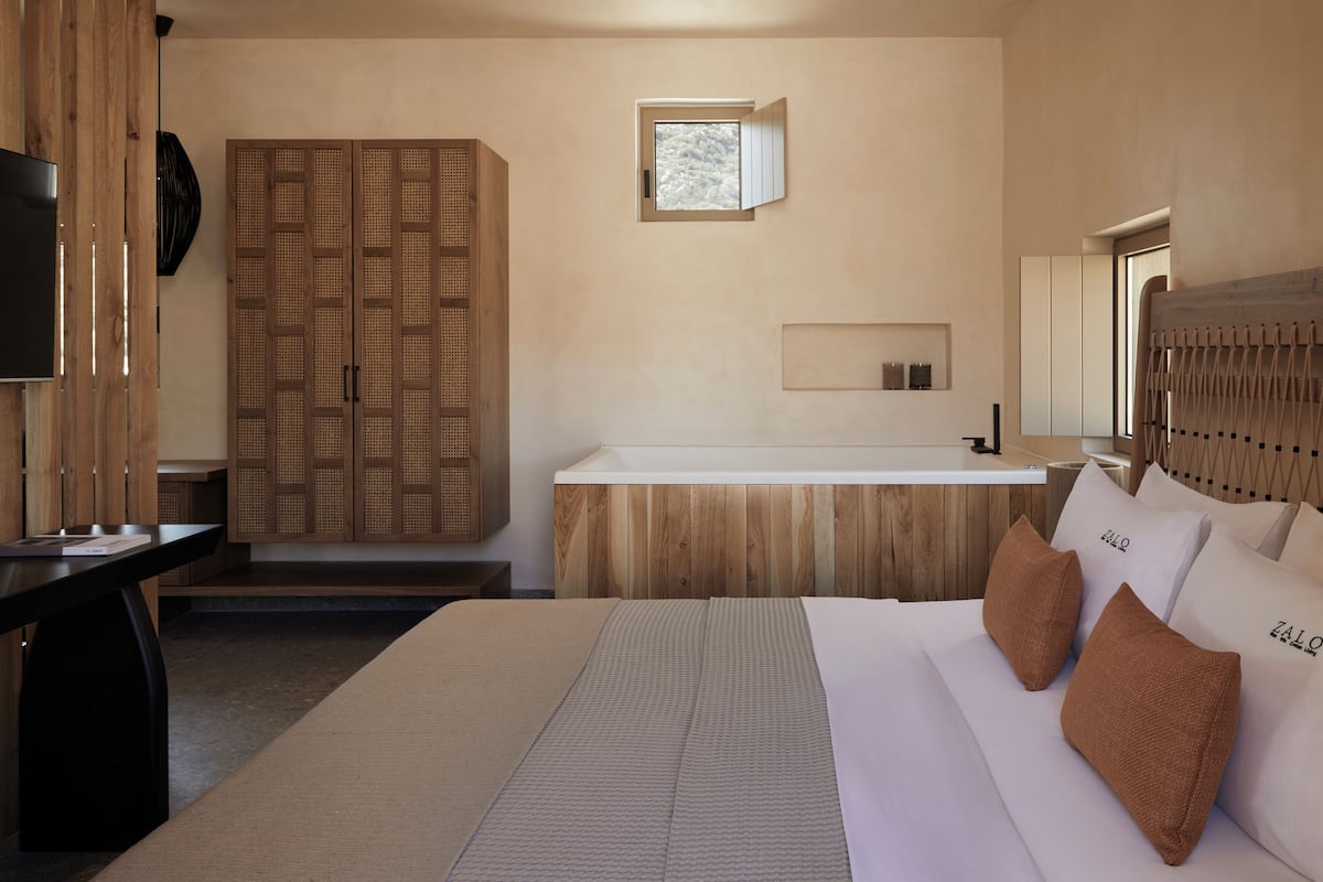 Un dormitorio con una cama grande, un armario de madera, un ventanal pequeño y una mesita de noche.
