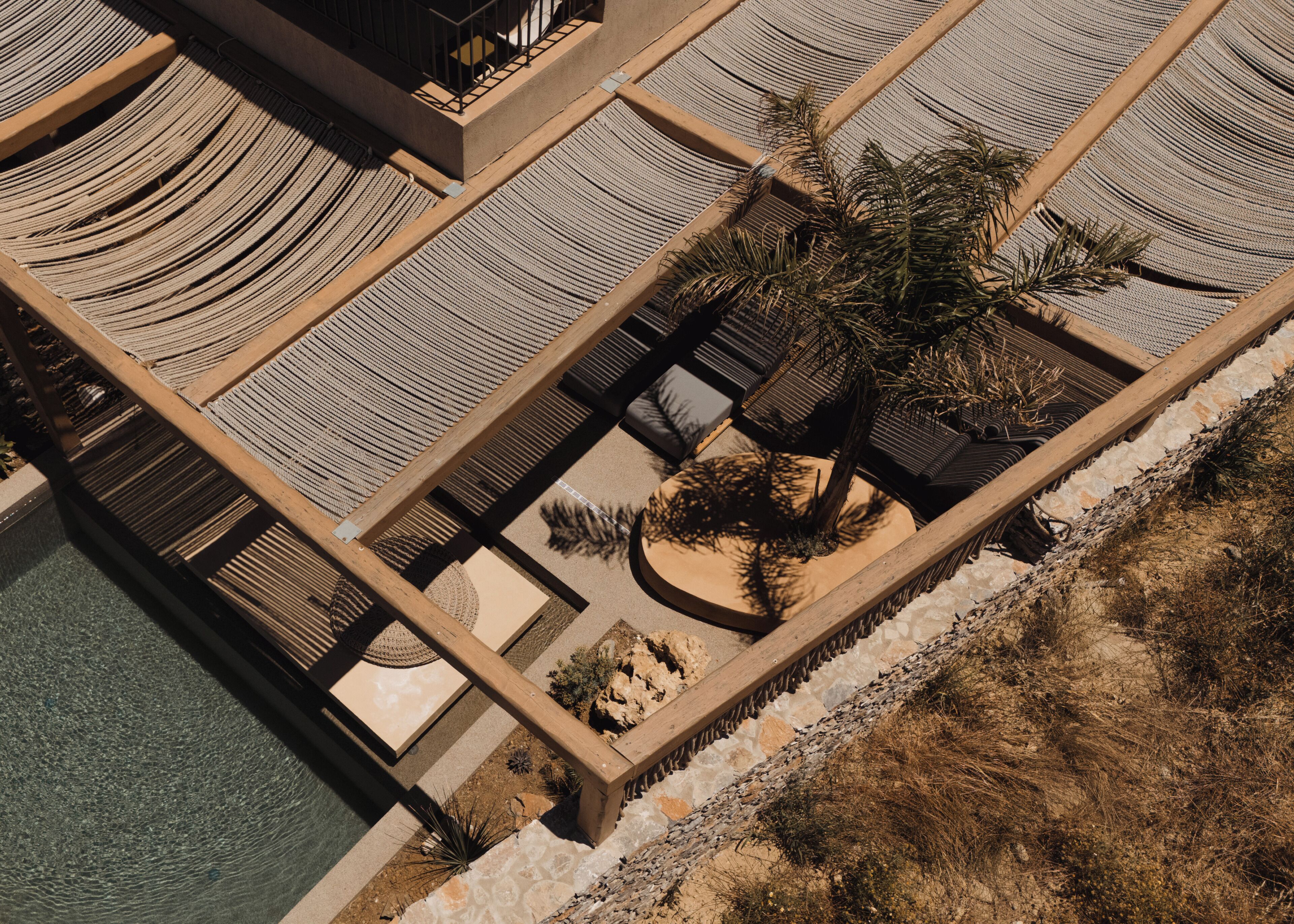 Vista aérea de un resort con múltiples camastros, una palmera y un área de piscina.
