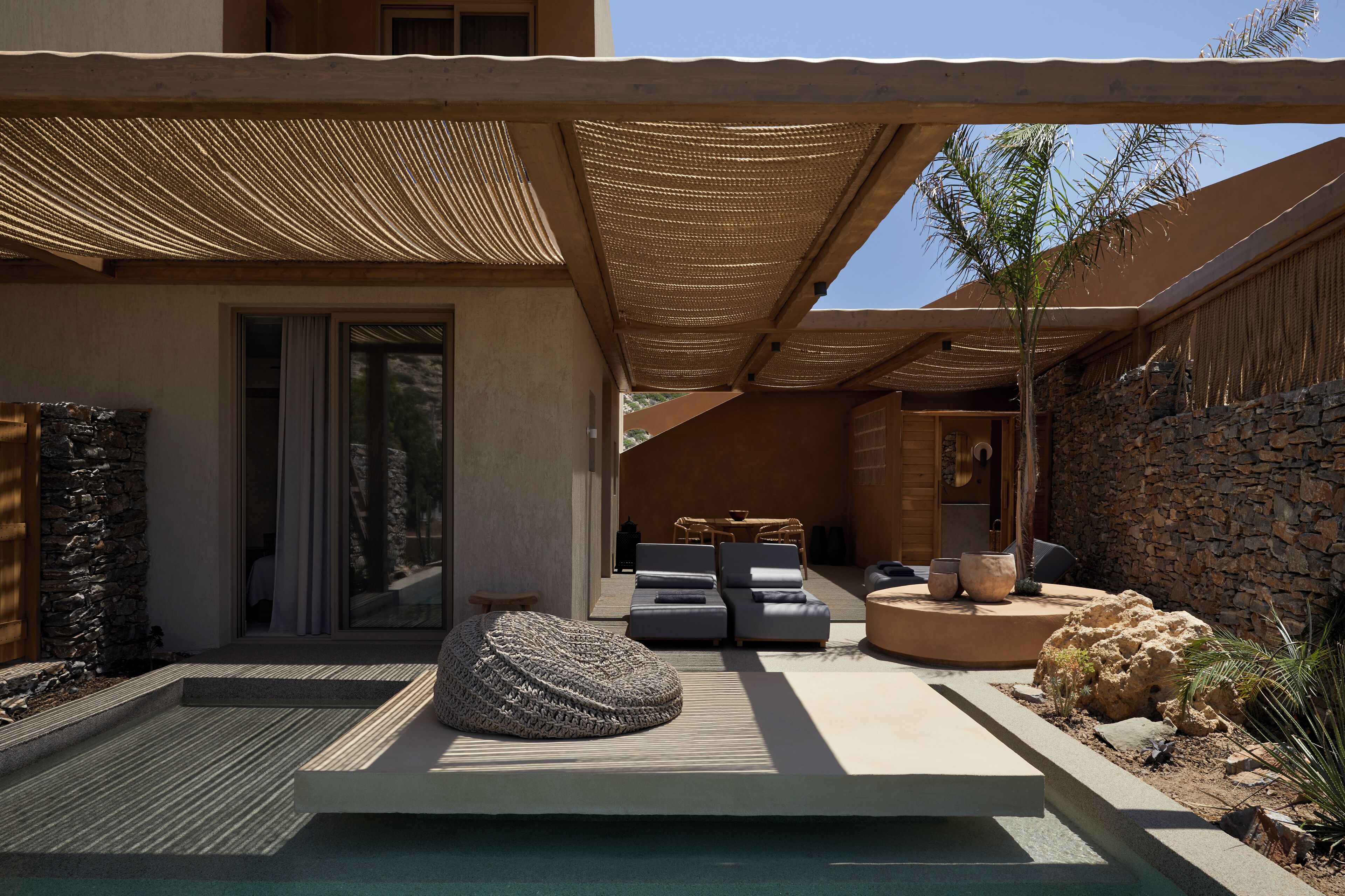 Un área exterior moderna con muro de piedra, piscina y mobiliario exterior.