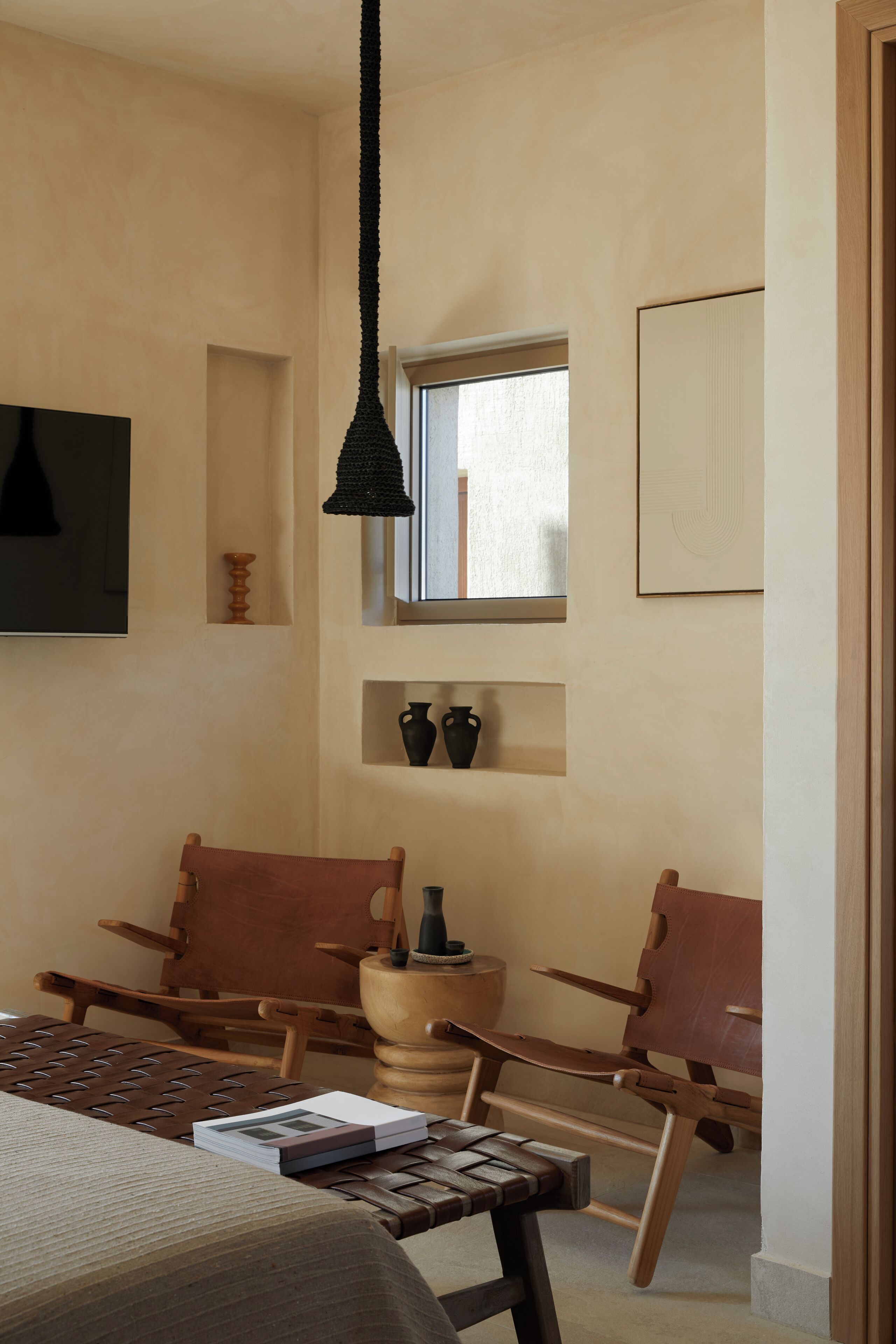 Un dormitorio con una cama, dos sillas de madera, una mesita, un candelabro colgante y una ventana con vistas.