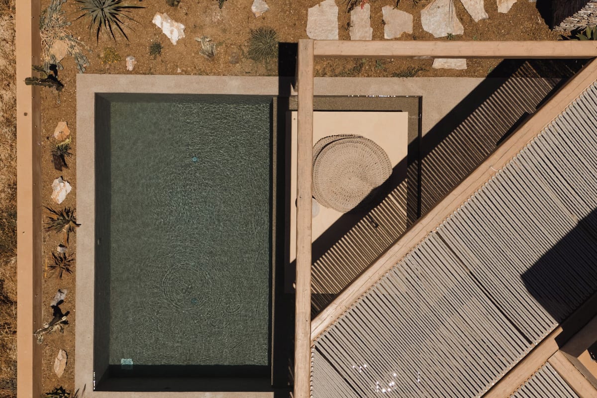 Vista aérea de un resort con piscina, tumbonas y un muro de piedra.