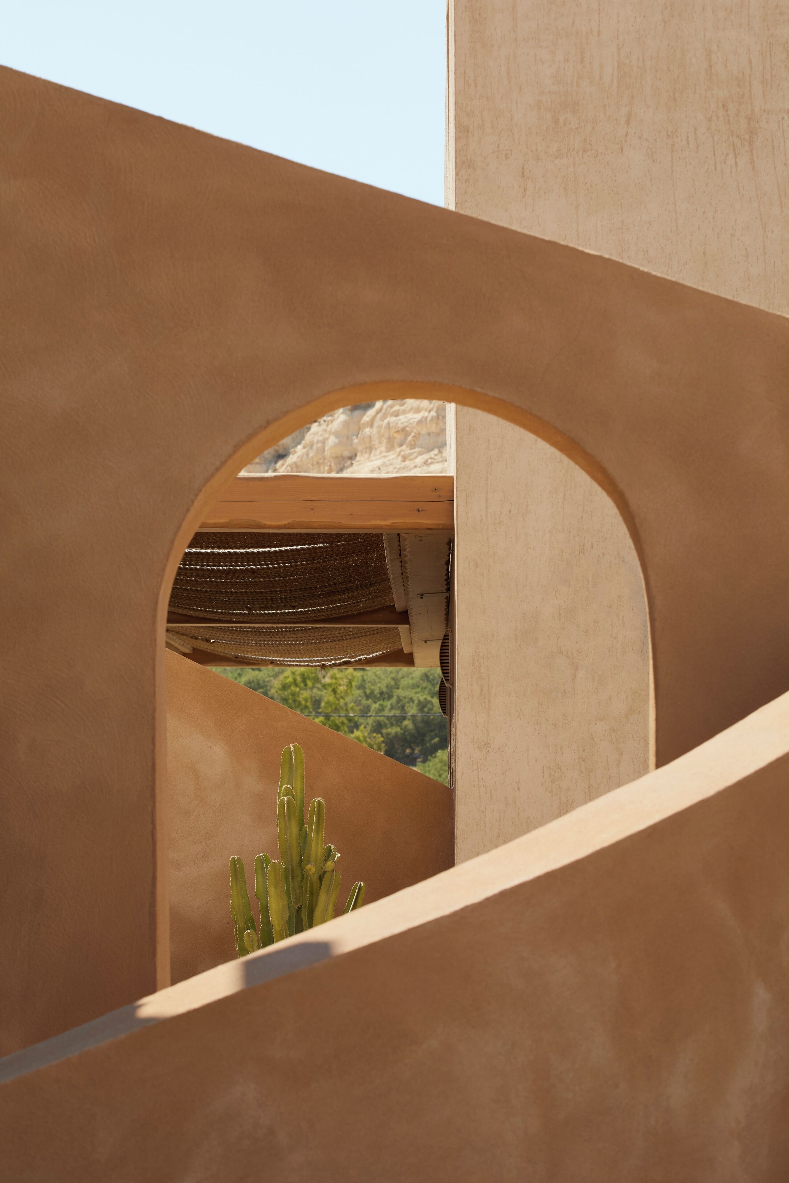 A building with a curved archway, a cactus, and a view of greenery.