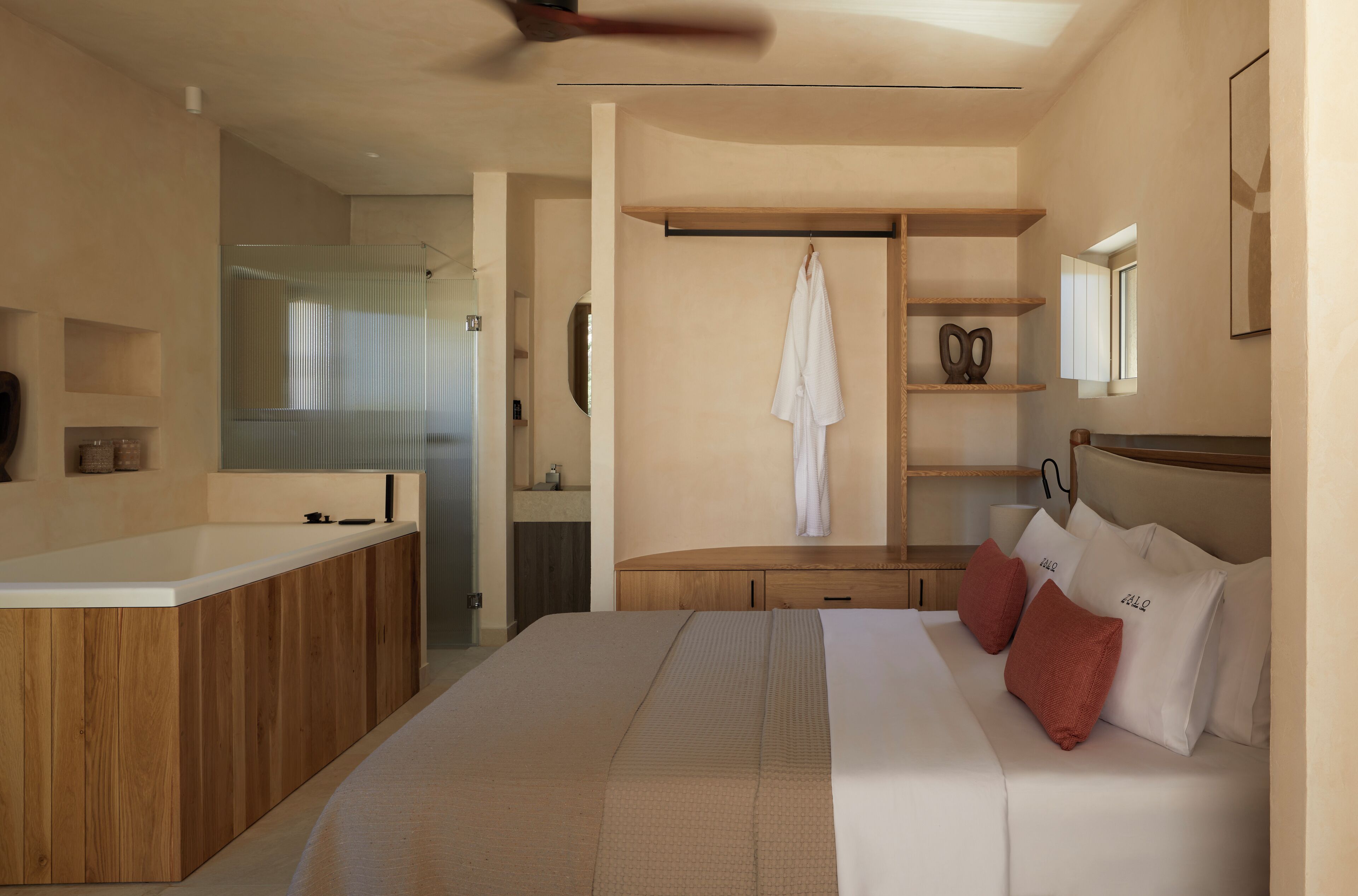 Une chambre d’hôtel moderne avec une coiffeuse en bois, un grand lit avec des oreillers rouges et une étagère intégrée où est accrochée une serviette.