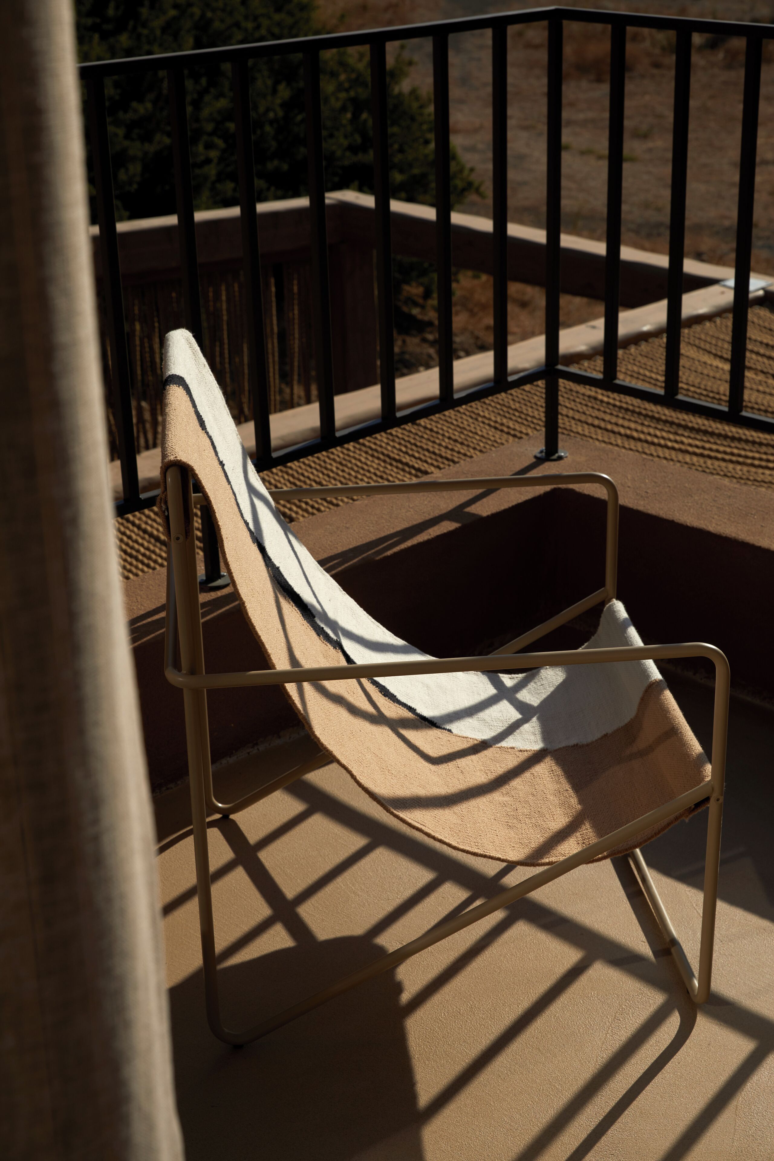 Ein Loungesessel mit Metallgestell und beiger Polsterung auf einem Balkon.