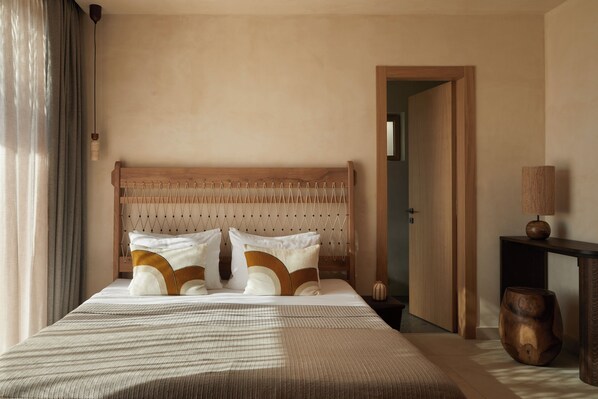 A neatly made bed with a wooden headboard, a bedside table with a lamp, and a wooden side table. - ADĀMA - A Signature Collection by Zálo Spaces (Adults Only) (Faistos)