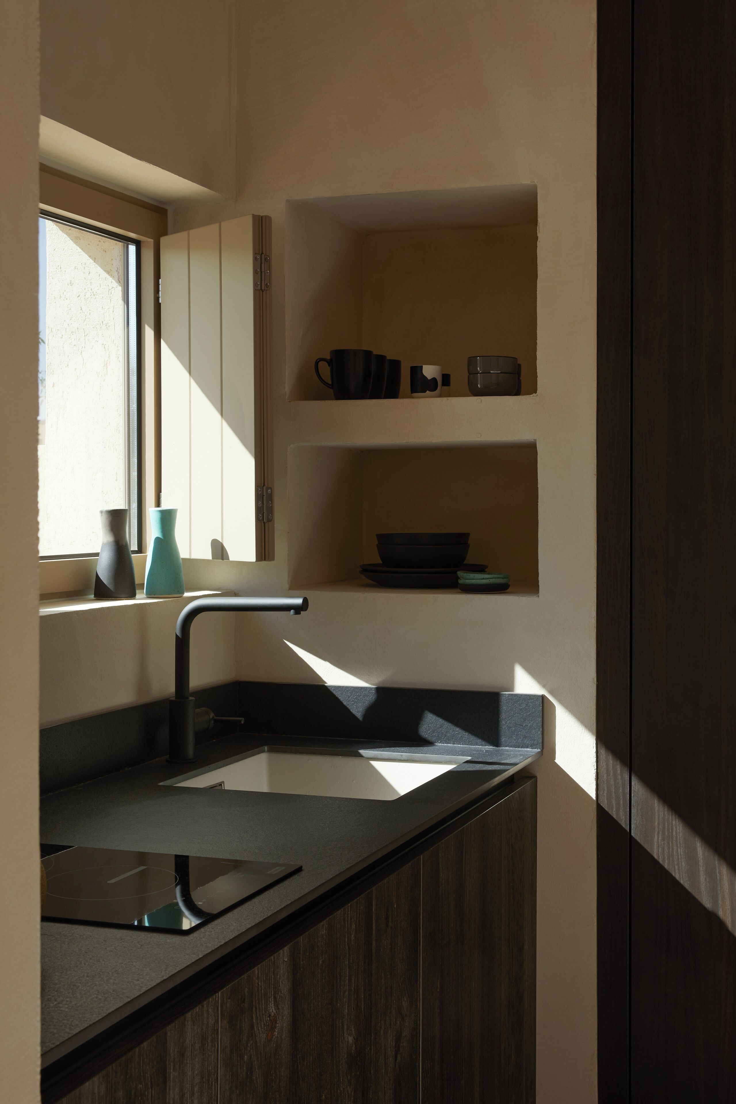 A modern kitchen with a built-in sink, a window, and a shelf with kitchenware.