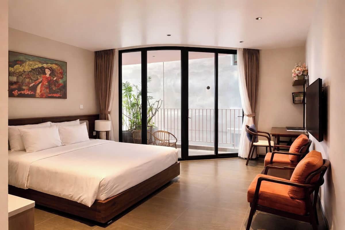 Habitación de hotel con cama, escritorio, silla, televisión y balcón con vistas.