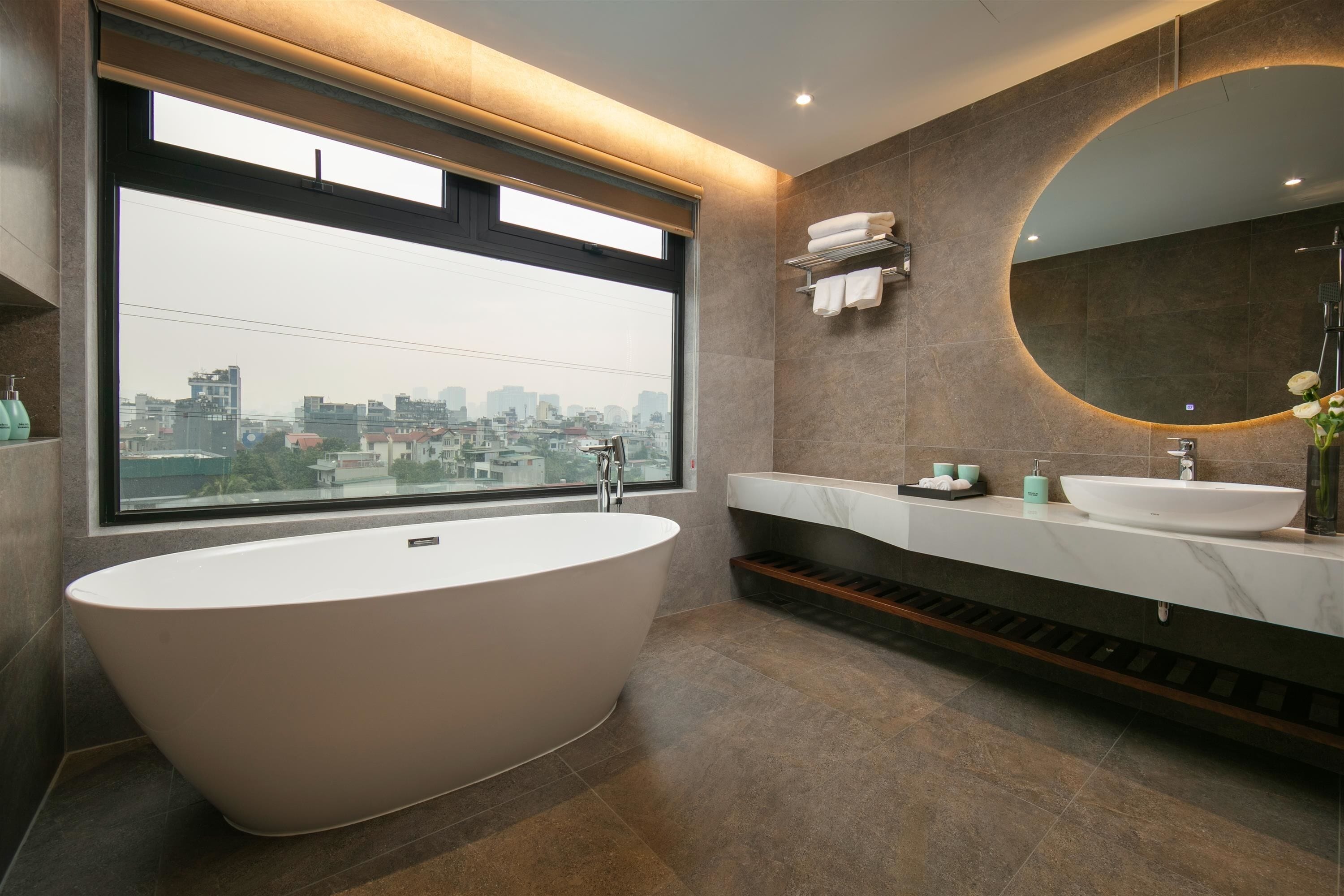 A modern bathroom with a freestanding bathtub, a large window, and a city view.