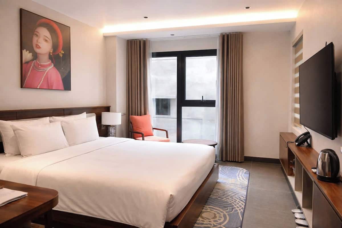 Habitación de hotel con una cama grande, un escritorio, una silla, un televisor y una ventana con cortinas.
