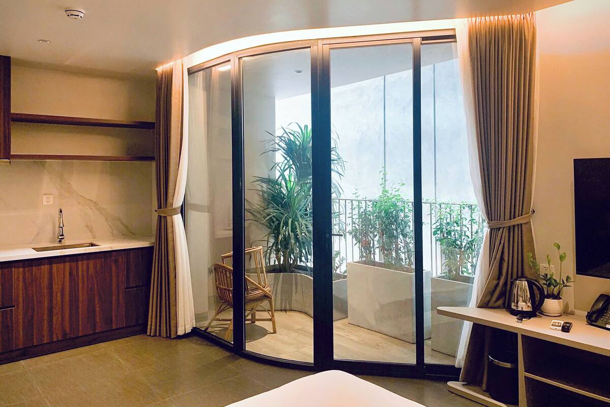 Una cocina moderna con un lavamanos, armarios de madera y un ventanal que da a un balcón con plantas y una silla.