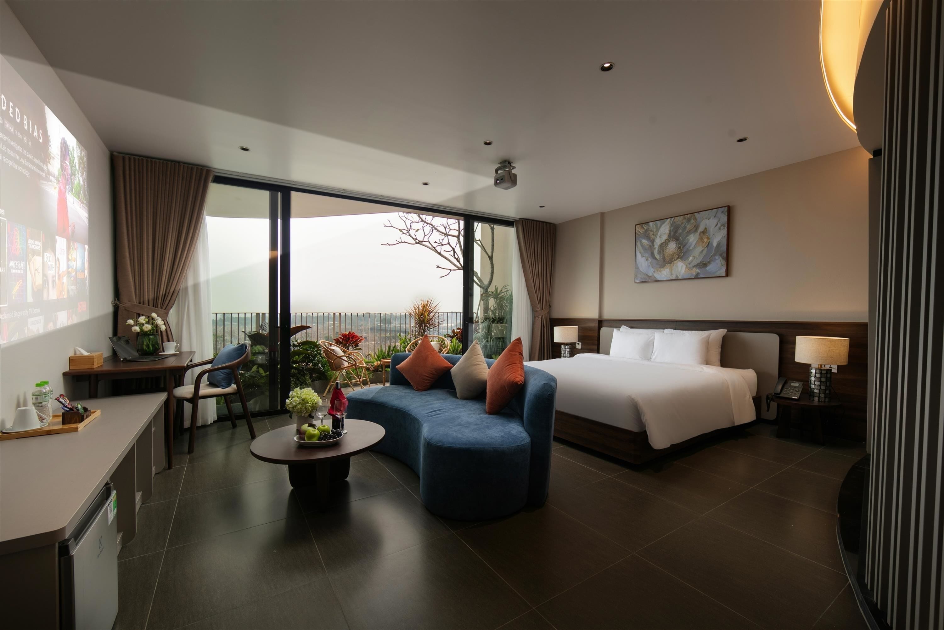 A hotel room with a bed, a sofa, a dining area, and a balcony with a view.
