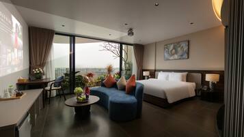 A hotel room with a bed, a sofa, a dining area, and a balcony with a view.