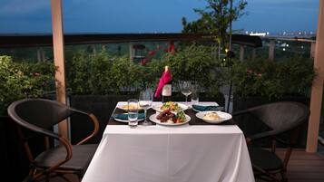 An outdoor dining table set with plates, glasses, and a bottle of wine, surrounded by wicker chairs.
