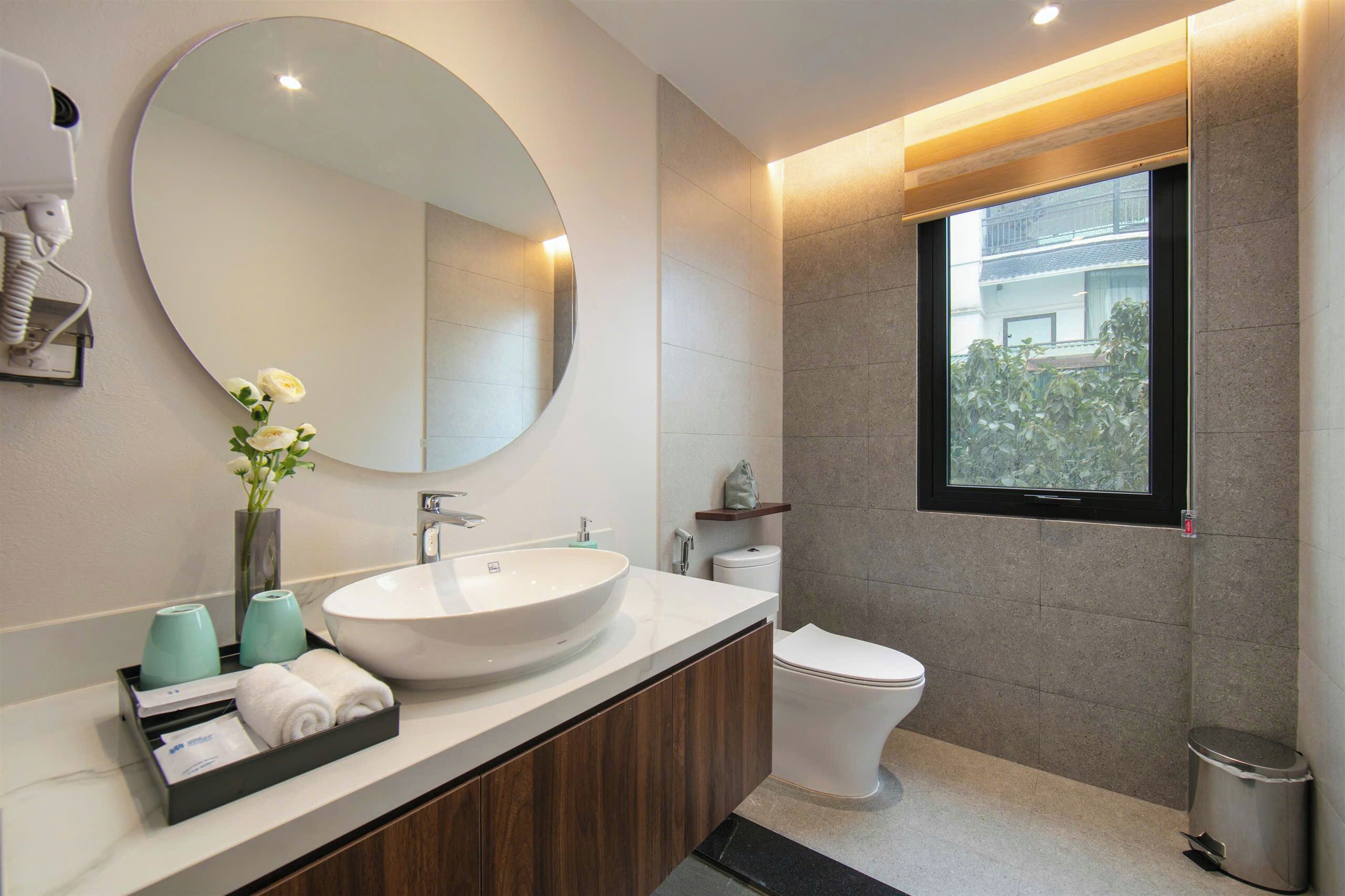 Un baño moderno con un espejo redondo, un lavabo grande, un inodoro y una ventana.