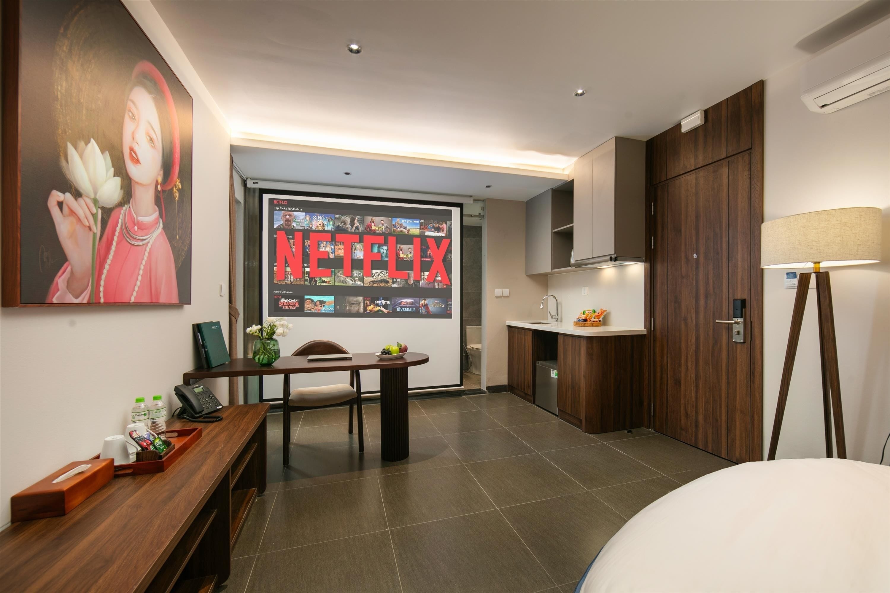 Une chambre d’hôtel équipée d’un lit, d’un bureau, d’une petite kitchenette, d’un téléviseur fixé au mur diffusant du contenu Netflix et d’un tableau accroché au mur.
