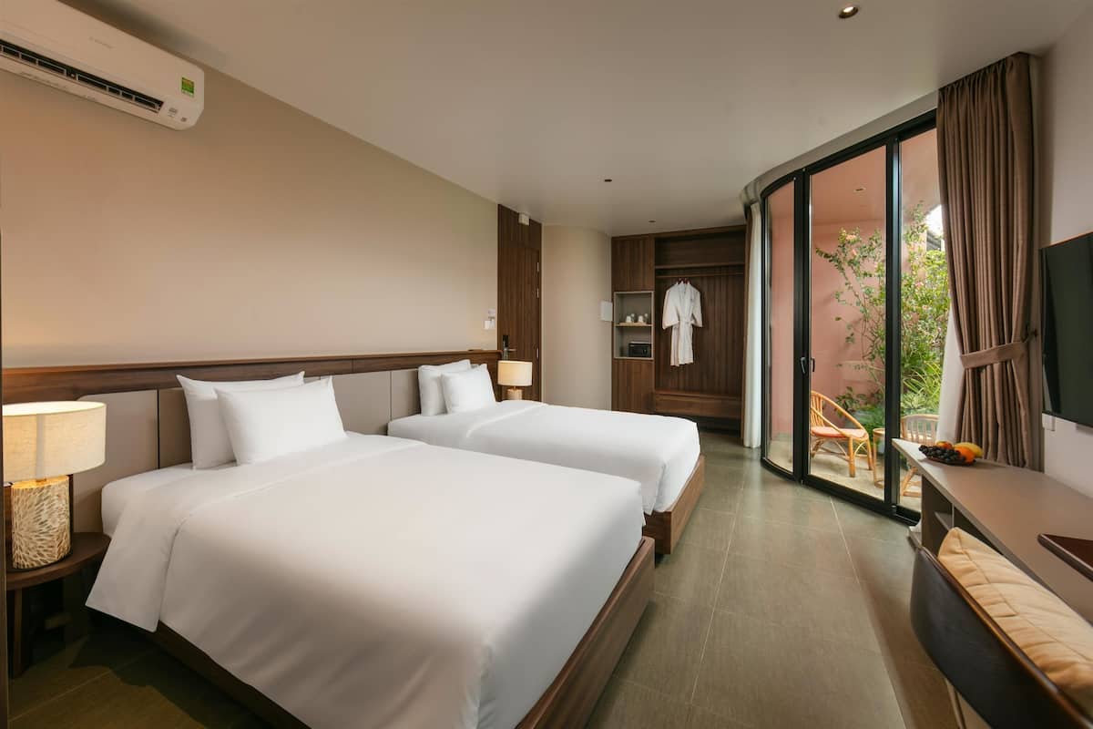 Habitación de hotel con dos camas, televisor, escritorio y balcón con una silla y una mesa.