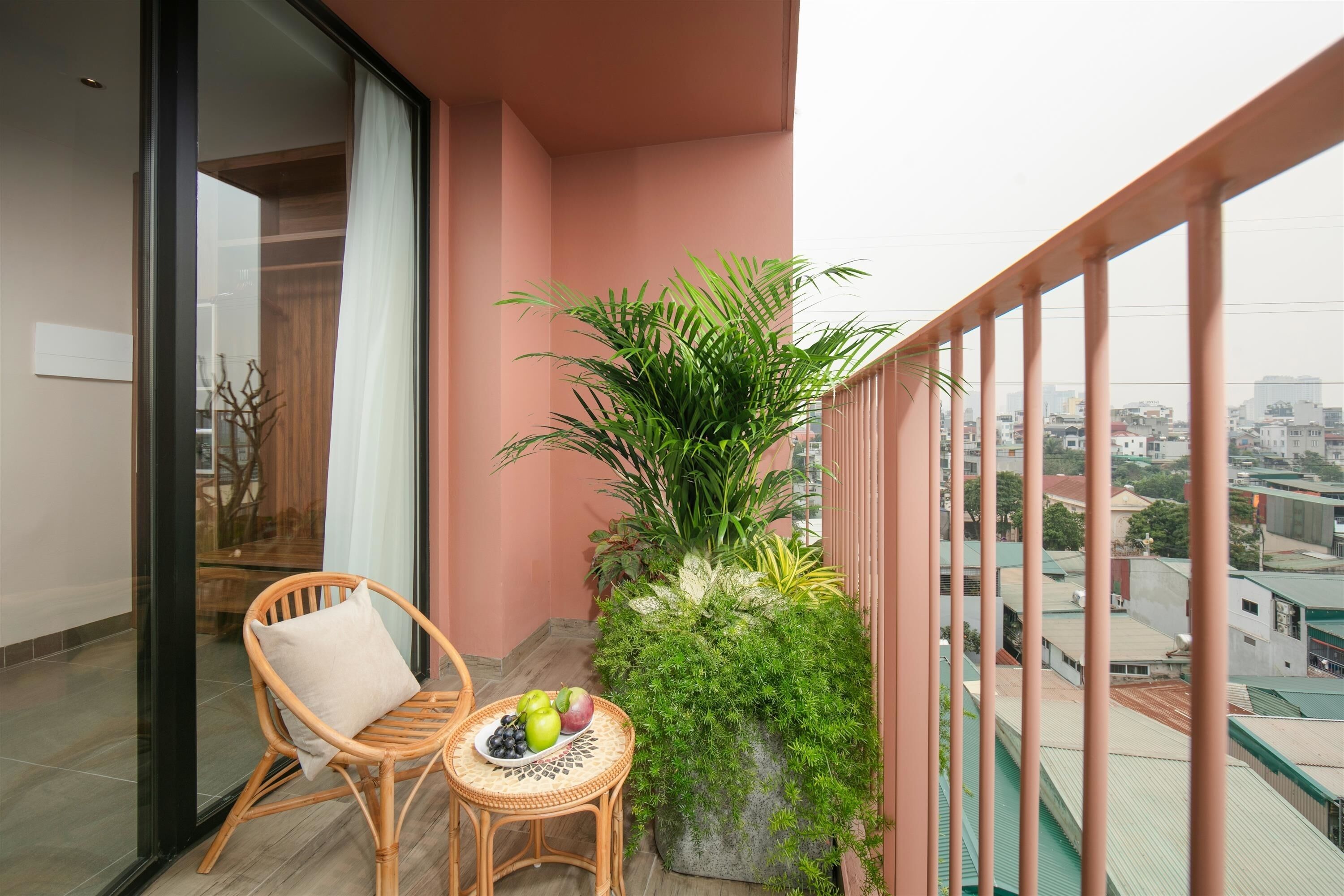 A balcony with a wicker chair, a small table with fruits, and a large potted plant.