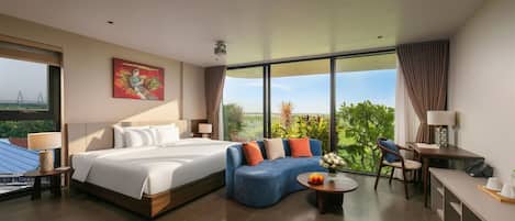 Een moderne hotelkamer met een groot bed, een blauwe bank, een bureau en uitzicht op groen.