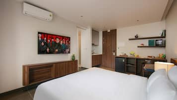 A hotel room with a large bed, a kitchenette, a wooden cabinet, a wall-mounted air conditioner, and a framed picture on the wall.