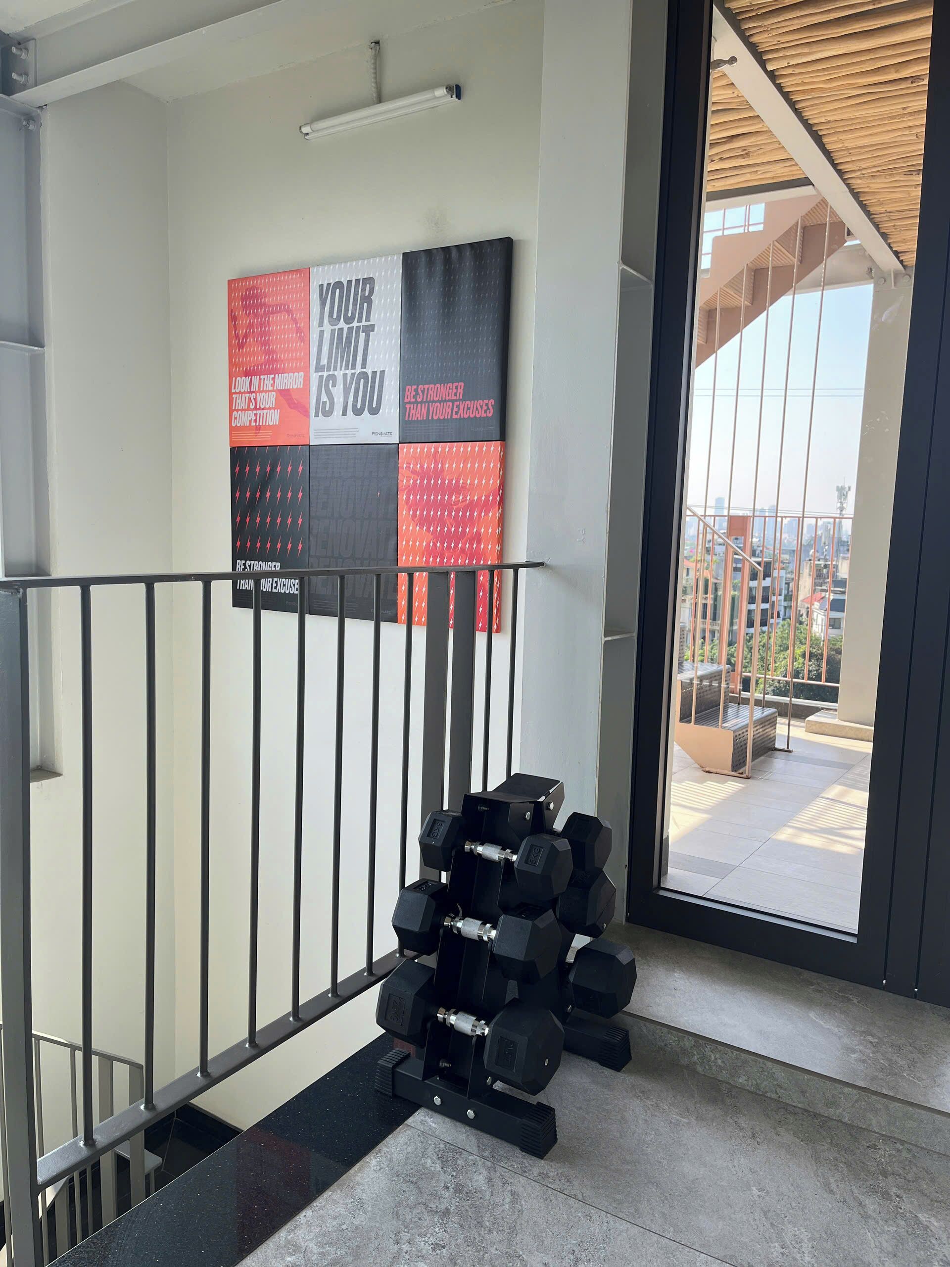 Et fitnessområde med en motiverende plakat, en trappe og udsigt over byen gennem en glasdør.
