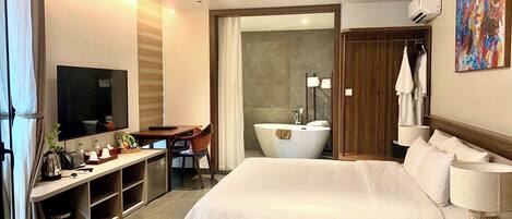 A hotel room with a bed, desk, chair, TV, bathroom, and artwork.