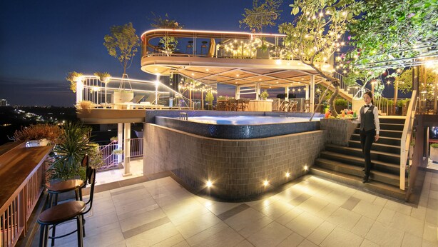 Un área de bar moderna al aire libre con jacuzzi, asientos y una escalera que lleva a una terraza superior.