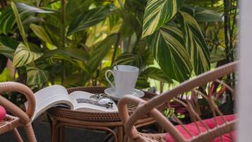 A wicker chair with a book and a cup on a table, surrounded by lush green plants.