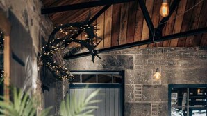 Ein rustikales Interieur mit freiliegenden Backsteinwänden, Holzbalkendecke, einem großen Fenster und einer Sitzecke mit Stuhl und Tisch.