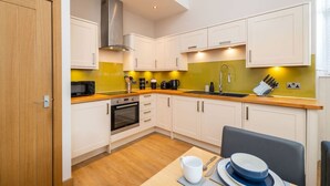 A compact kitchen with white cabinets, a stainless steel range hood, a built-in oven, a sink with a modern faucet, and a wooden countertop.