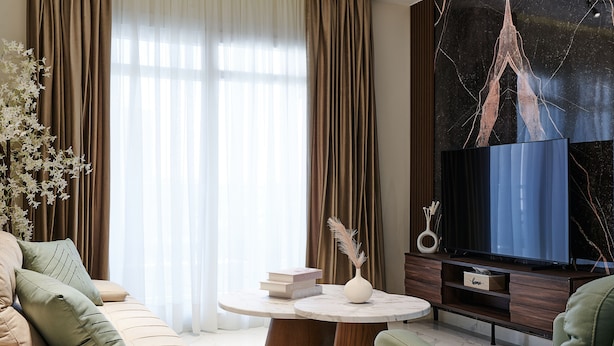 Una sala de estar moderna con un sofá, una mesa de centro con libros y un jarrón, un televisor de pantalla plana y un adorno de pared.
