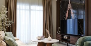 Un salon moderne comprenant un canapé, une table basse avec des livres et un vase, un téléviseur à écran plat et un élément décoratif mural.