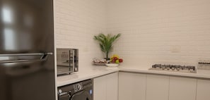 Una cocina con microondas, tostadora y estufa a gas. Hay un escurreplatos y un tazón de fruta en la encimera.