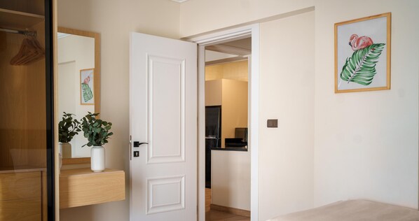 Une pièce avec une porte blanche, une commode en bois, une plante en pot et un tableau encadré au mur.