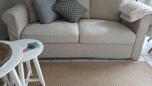 Un canapé beige avec deux coussins, une table blanche avec des magazines et un tapis tissé.