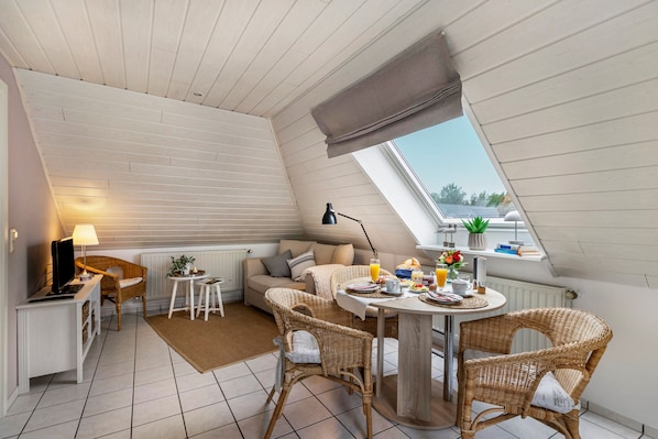 A cozy loft bedroom with a sloped ceiling, a dining area with wicker furniture, and a view through a skylight.