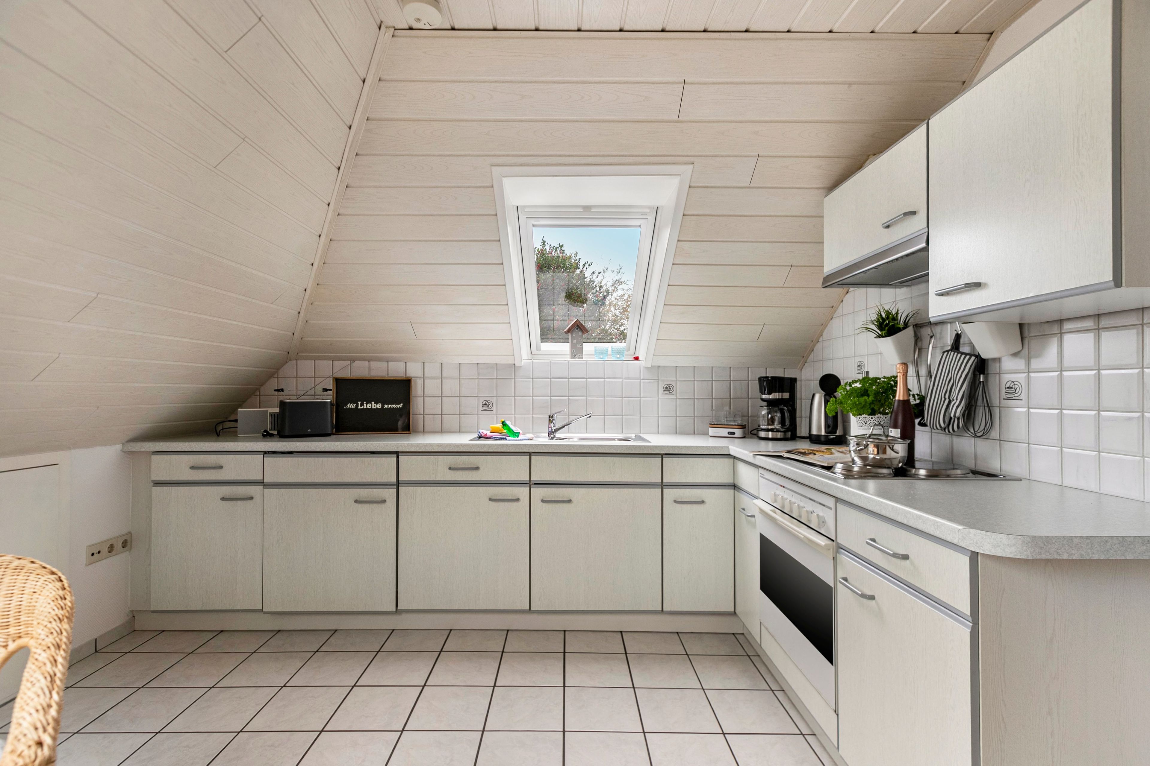 Een kleine keuken met een schuine kap, een raam en een inbouwoven.