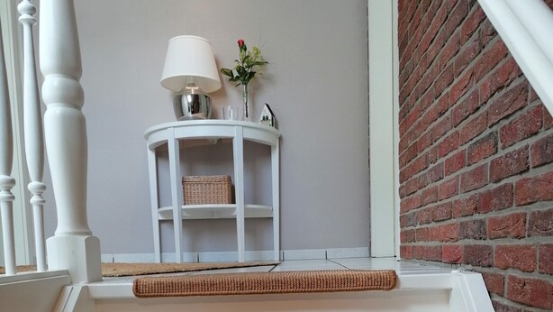 Un escalier à trois marches, chacune recouverte d’un tapis tissé. Une lampe blanche et une petite table sur laquelle est posé un vase de fleurs se trouvent sur le palier.