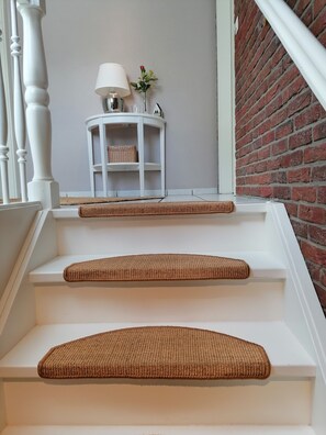 A staircase with three steps, each with a woven mat. A white lamp and a small table with a vase of flowers are on the landing.