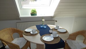Une table de salle à manger ronde, entourée de quatre chaises en osier, un pot de fleurs et un petit bouquet sur le rebord de la fenêtre.